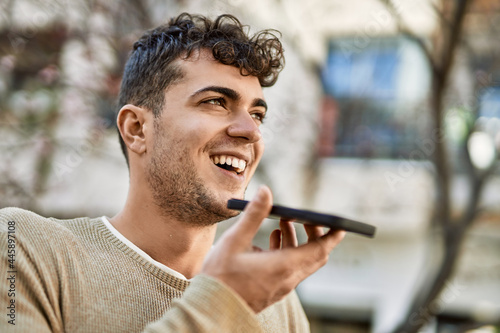 Young hispanic man sending voice message using smartphone at the city