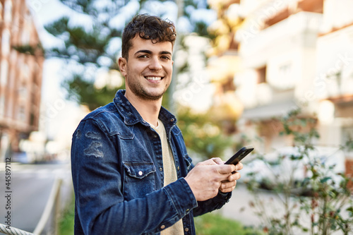 Young hispanic man smiling happy using smartphone at the city