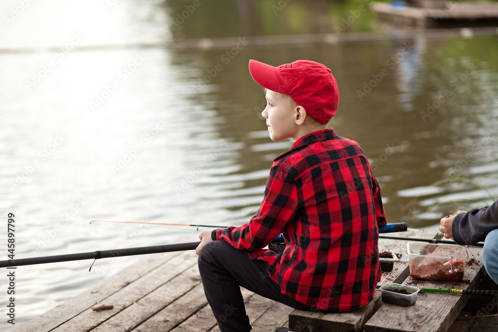 Cute boy in checkered shirt fishing on the lake. Summer outdoor activity concept.
