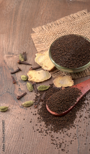 Black Tea Powder or dry dust tea powder, chai patti isolated in wooden bowl with Cardamom, Clove and Ginger.