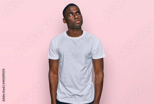 Young african american man wearing casual white t shirt smiling looking to the side and staring away thinking.