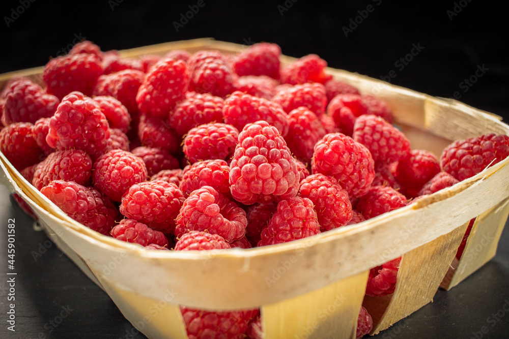 Raspberries in wooden basket on black stone background