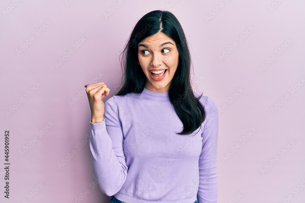 Young hispanic woman wearing casual clothes smiling with happy face looking and pointing to the side with thumb up. Young hispanic woman wearing casual clothes smiling with happy face looking and pointing to the side with thumb up.
