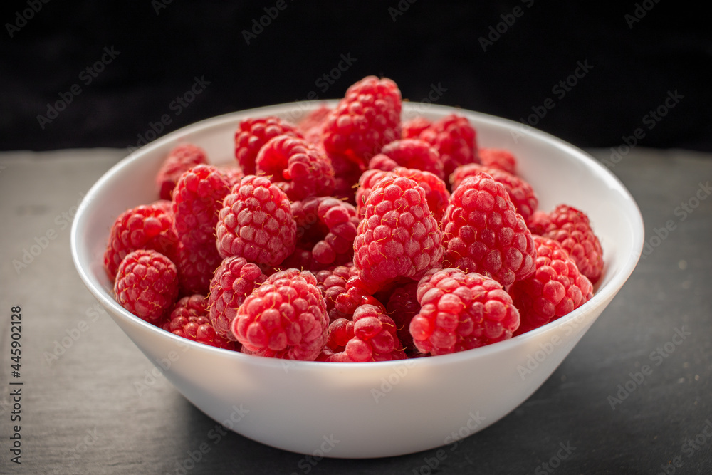 Raspberries in white bowl on black stone background Raspberries in white bowl on black stone background