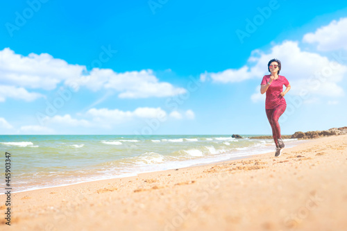 Asian woman in red workout clothes running on the beach in the morning