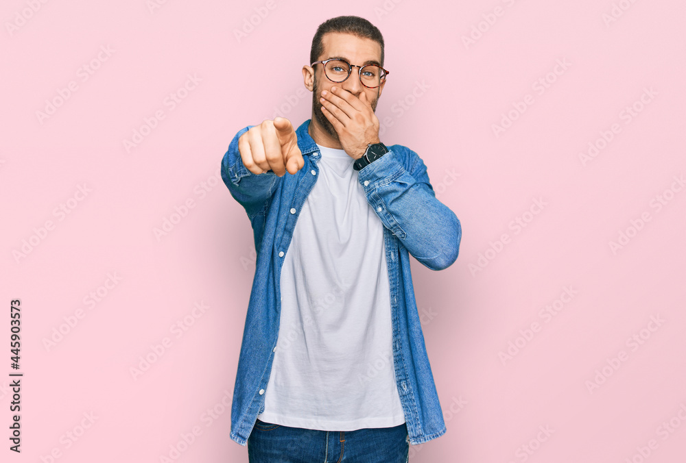 Young caucasian man wearing casual clothes laughing at you, pointing finger to the camera with hand over mouth, shame expression Young caucasian man wearing casual clothes laughing at you, pointing finger to the camera with hand over mouth, shame expression