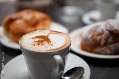 Traditional Italian breakfast. Fresh croissants with cream and sugar powder, espresso coffee and cappuccino on a black wooden table in Milan, Lombardy, Italy. European food and pastry.