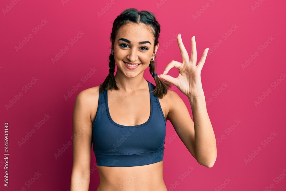 Young brunette girl wearing sportswear and braids smiling positive doing ok sign with hand and fingers. successful expression.