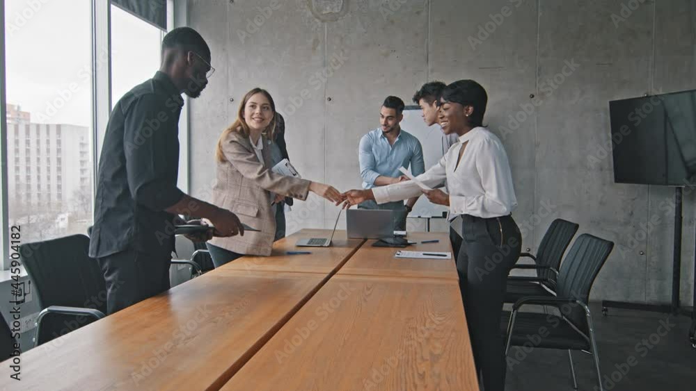Multiracial group of colleagues multiethnic corporate workers shaking hands making handshake greeting gesture meeting in office conference sitting down at table listening report of hispanic boss man