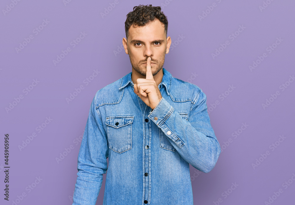 Obraz premium Young hispanic man wearing casual denim jacket asking to be quiet with finger on lips. silence and secret concept.