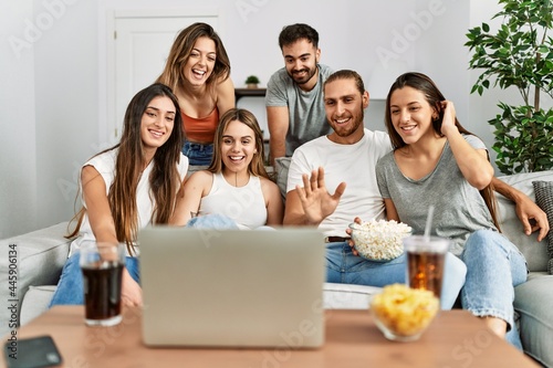 Group of young friends having video call using laptop sitting on the sofa at home.