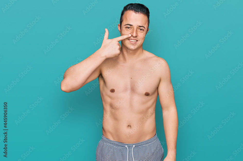 Fototapeta premium Handsome young man wearing swimwear shirtless pointing with hand finger to face and nose, smiling cheerful. beauty concept