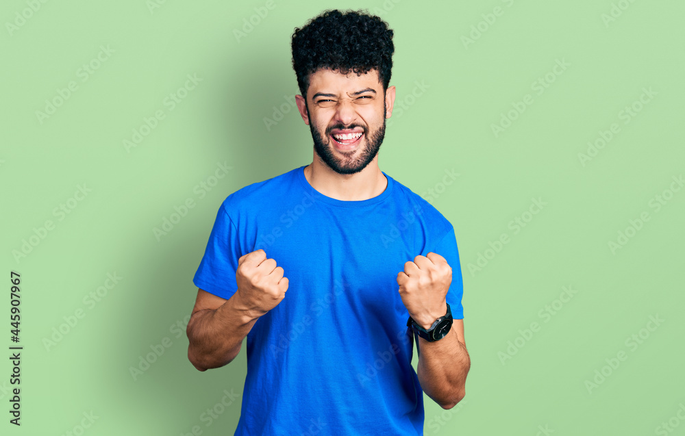 Young arab man with beard wearing casual blue t shirt celebrating surprised and amazed for success with arms raised and eyes closed. winner concept.