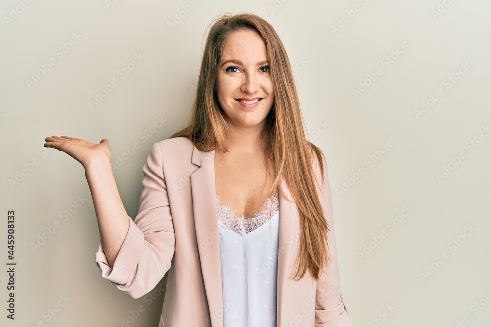 Young blonde woman wearing business jacket and glasses smiling cheerful presenting and pointing with palm of hand looking at the camera. Young blonde woman wearing business jacket and glasses smiling cheerful presenting and pointing with palm of hand looking at the camera.