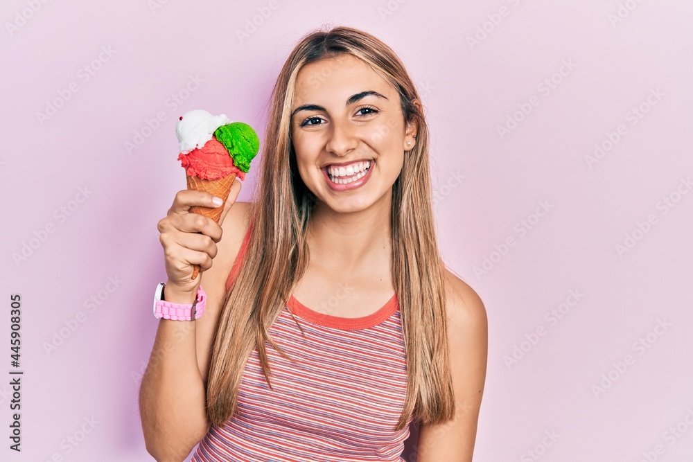 Beautiful hispanic woman holding ice cream looking positive and happy standing and smiling with a confident smile showing teeth Beautiful hispanic woman holding ice cream looking positive and happy standing and smiling with a confident smile showing teeth