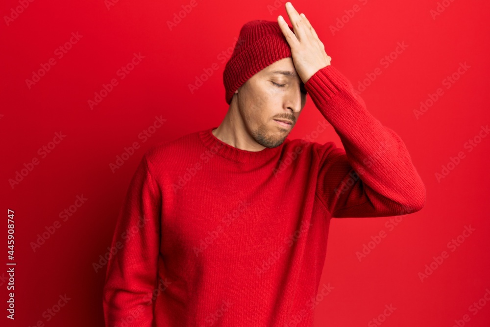 Bald man with beard wearing wool sweater and winter hat surprised with hand on head for mistake, remember error. forgot, bad memory concept. Bald man with beard wearing wool sweater and winter hat surprised with hand on head for mistake, remember error. forgot, bad memory concept.