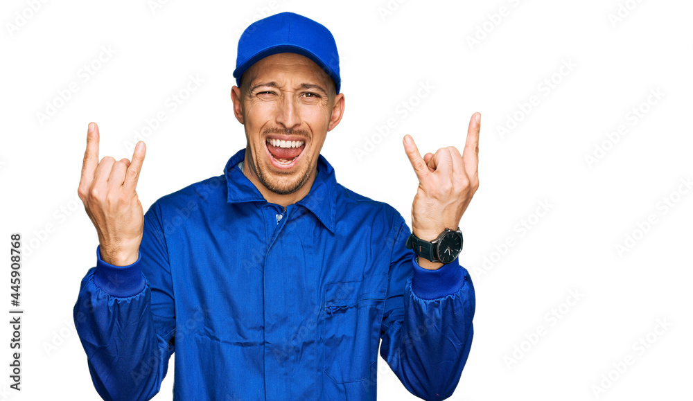 Bald man with beard wearing builder jumpsuit uniform shouting with crazy expression doing rock symbol with hands up. music star. heavy music concept. Bald man with beard wearing builder jumpsuit uniform shouting with crazy expression doing rock symbol with hands up. music star. heavy music concept.
