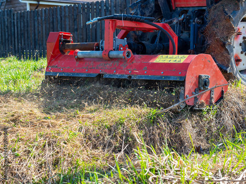 a tractor with a mower attached mulches dry grass along the fence. Land plot processing