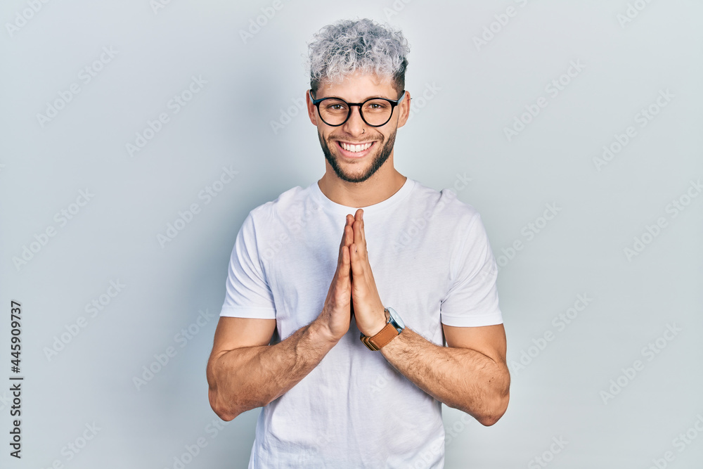 Young hispanic man with modern dyed hair wearing white t shirt and glasses  praying with hands together asking for forgiveness smiling confident. Stock  Photo | Adobe Stock
