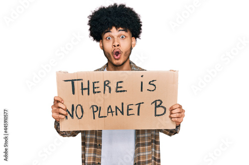 Young african american man with afro hair holding there is no planet b banner scared and amazed with open mouth for surprise, disbelief face © Krakenimages.com
