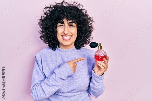 Young middle east woman holding perfume smiling happy pointing with hand and finger