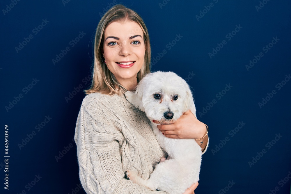 Beautiful caucasian woman hugging cute dog looking positive and happy standing and smiling with a confident smile showing teeth Beautiful caucasian woman hugging cute dog looking positive and happy standing and smiling with a confident smile showing teeth