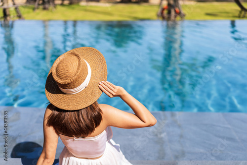 Young woman traveler relaxing and enjoying by a tropical resort pool while traveling for summer vacation