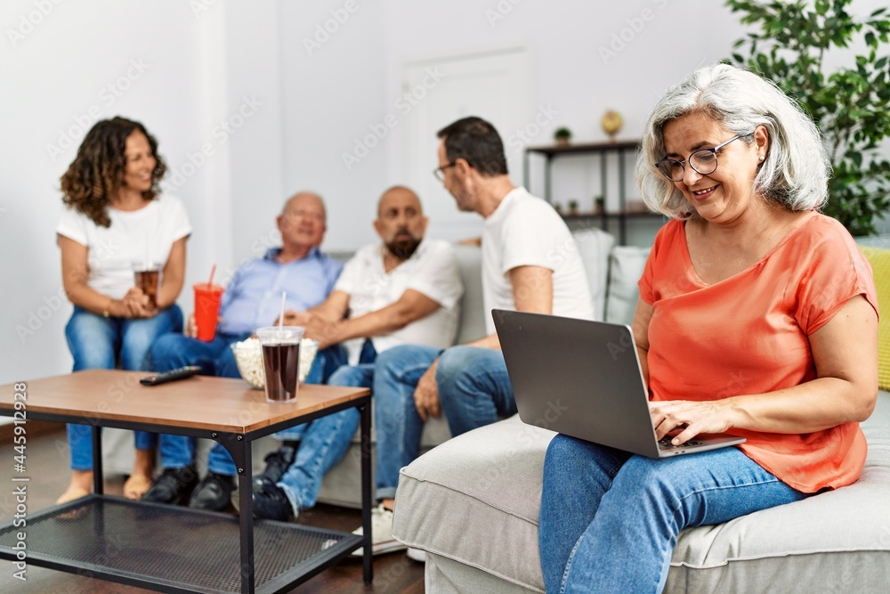 Group of middle age friends sitting on the sofa speaking. Woman smiling happy using laptop at home. Group of middle age friends sitting on the sofa speaking. Woman smiling happy using laptop at home.