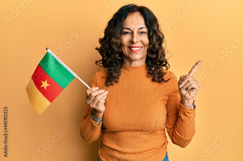 Middle age hispanic woman holding cameroon flag smiling happy pointing with hand and finger to the side