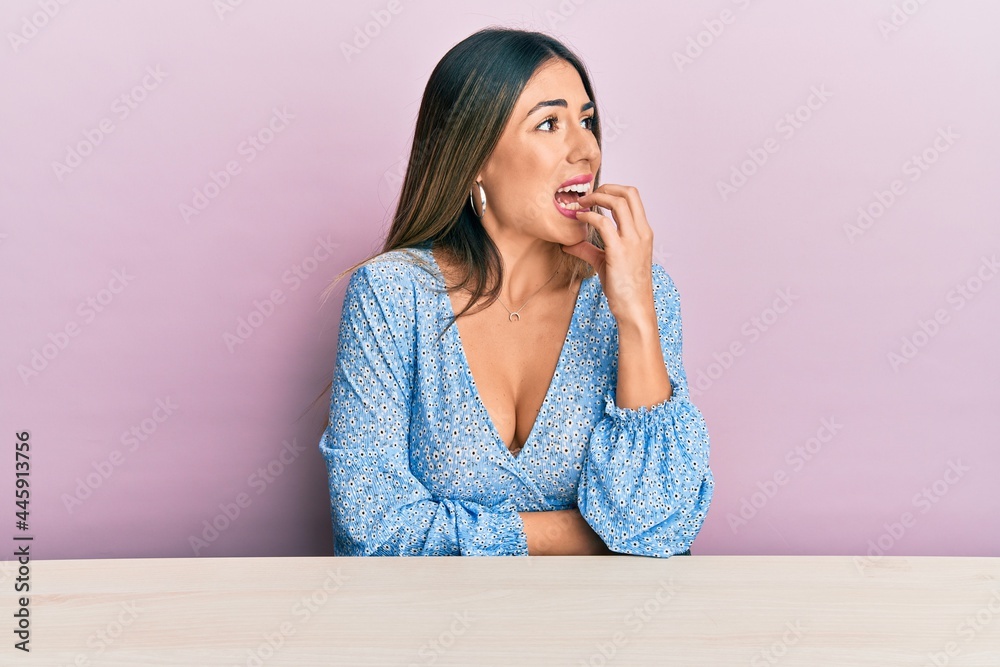 Young hispanic woman wearing casual clothes sitting on the table looking stressed and nervous with hands on mouth biting nails. anxiety problem. Young hispanic woman wearing casual clothes sitting on the table looking stressed and nervous with hands on mouth biting nails. anxiety problem.