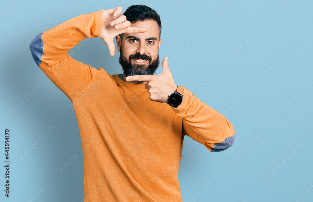 Naklejka premium Hispanic man with beard wearing casual winter sweater smiling making frame with hands and fingers with happy face. creativity and photography concept.