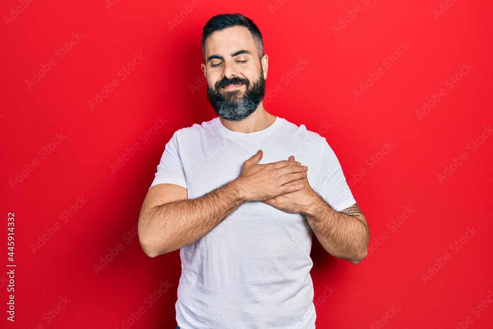Young hispanic man wearing casual white t shirt smiling with hands on chest, eyes closed with grateful gesture on face. health concept. Young hispanic man wearing casual white t shirt smiling with hands on chest, eyes closed with grateful gesture on face. health concept.