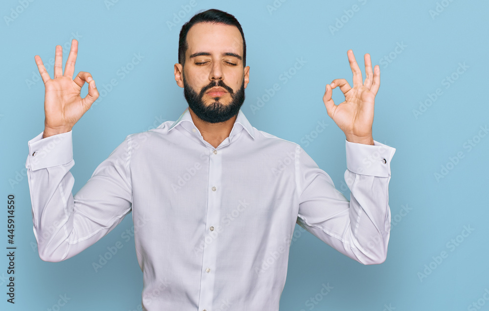 Young man with beard wearing business shirt relax and smiling with eyes closed doing meditation gesture with fingers. yoga concept. Young man with beard wearing business shirt relax and smiling with eyes closed doing meditation gesture with fingers. yoga concept.