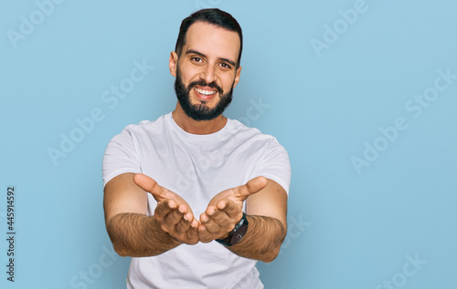 Young man with beard wearing casual white t shirt smiling with hands palms together receiving or giving gesture. hold and protection photo