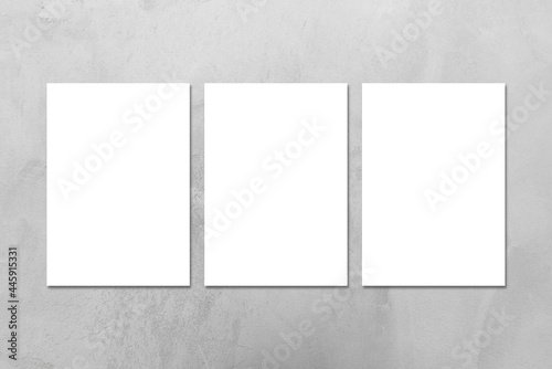 Three empty white vertical DIN A4 rectangle poster or business card mockups on the gray concrete stone wall.Flat lay, top view. For advertising, brand design, stationery presentation.