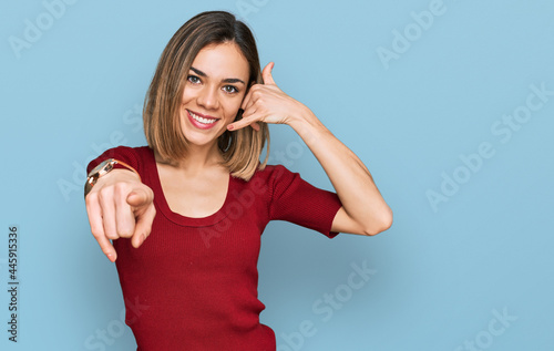 Young blonde girl wearing casual clothes smiling doing talking on the telephone gesture and pointing to you. call me.