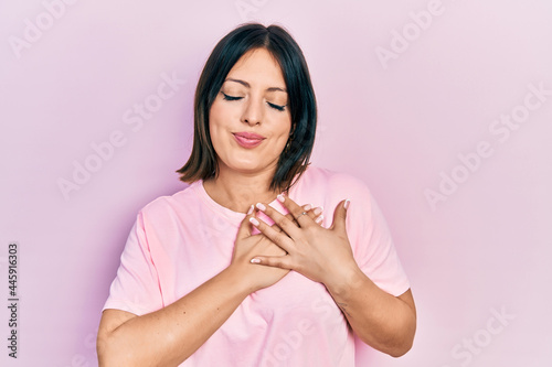 Young hispanic woman wearing casual pink t shirt smiling with hands on chest with closed eyes and grateful gesture on face. health concept.