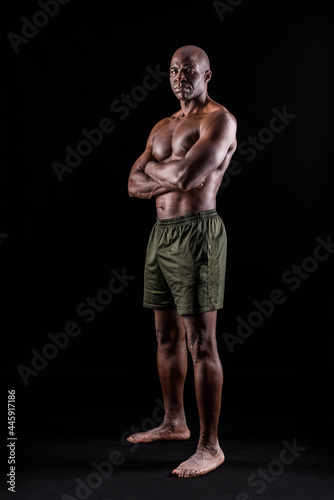 Black man in shorts standing with arms crossed looking at camera seriously 