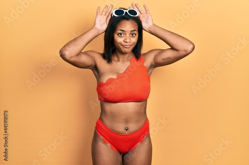 Young african american girl wearing bikini doing bunny ears gesture with hands palms looking cynical and skeptical. easter rabbit concept.