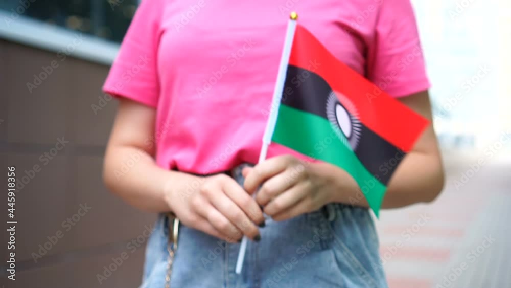 Unrecognizable woman holding Malawian flag. Girl walking down street with national flag of Malawi