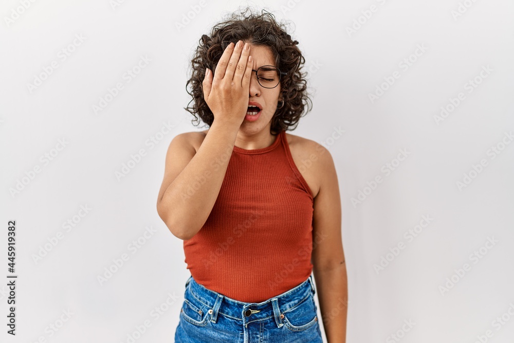 Young hispanic woman wearing glasses standing over isolated background yawning tired covering half face, eye and mouth with hand. face hurts in pain. Young hispanic woman wearing glasses standing over isolated background yawning tired covering half face, eye and mouth with hand. face hurts in pain.