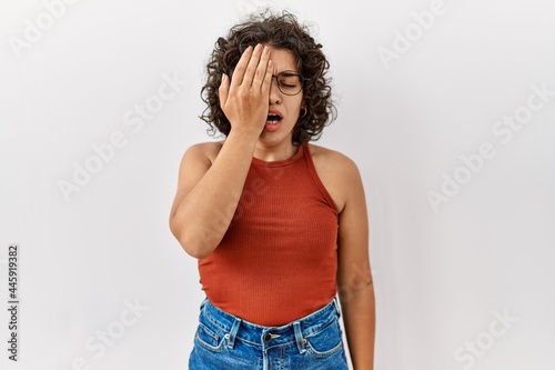 Young hispanic woman wearing glasses standing over isolated background yawning tired covering half face  eye and mouth with hand. face hurts in pain.