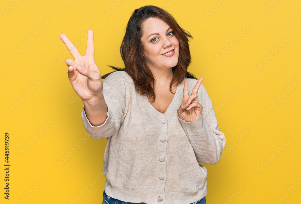 Young plus size woman wearing casual clothes smiling looking to the camera showing fingers doing victory sign. number two.