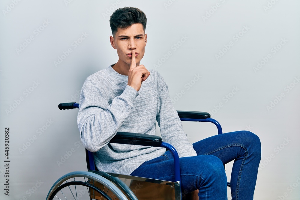 Young hispanic man sitting on wheelchair asking to be quiet with finger on lips. silence and secret concept. Young hispanic man sitting on wheelchair asking to be quiet with finger on lips. silence and secret concept.
