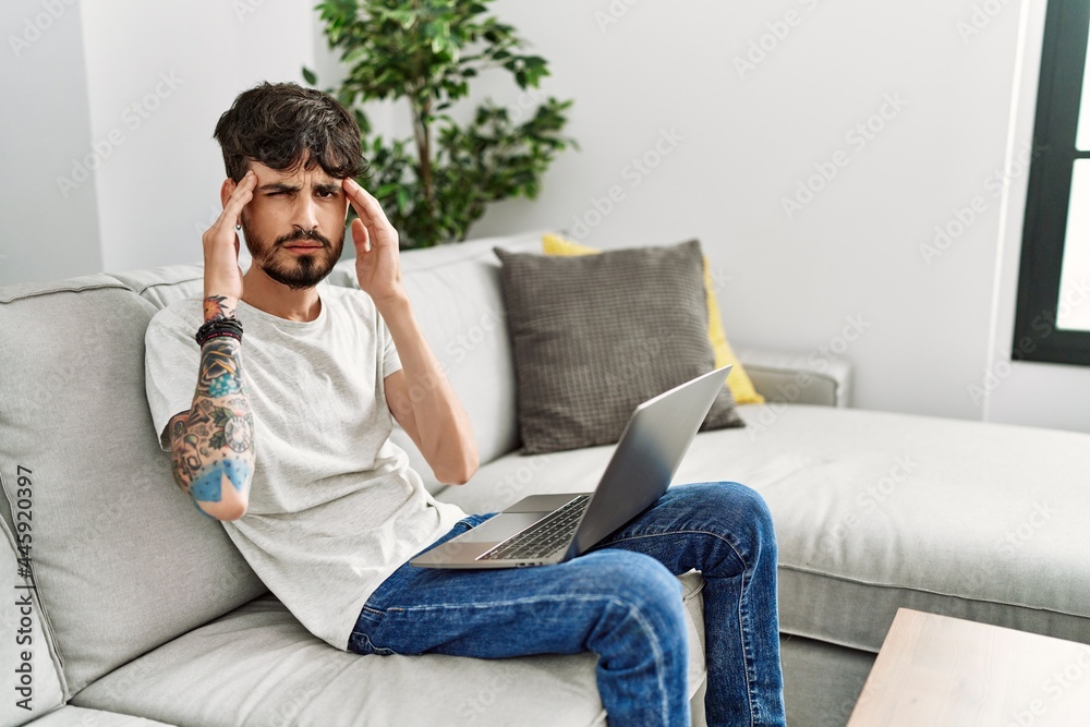Hispanic man with beard sitting on the sofa with hand on head for pain in head because stress. suffering migraine. Hispanic man with beard sitting on the sofa with hand on head for pain in head because stress. suffering migraine.