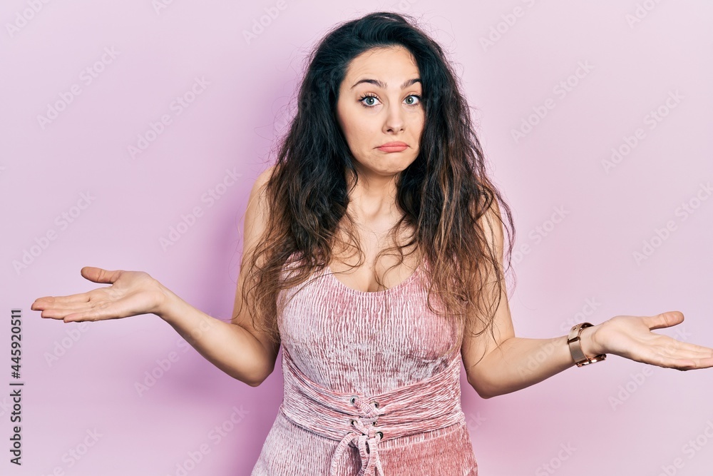 Young hispanic woman wearing casual clothes clueless and confused expression with arms and hands raised. doubt concept.