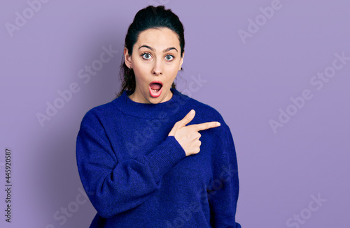 Young hispanic woman wearing casual clothes surprised pointing with finger to the side, open mouth amazed expression.