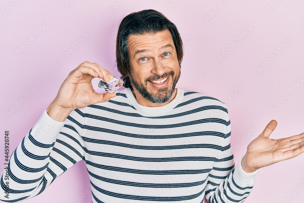 Fototapeta premium Middle age caucasian man holding brilliant diamond stone celebrating achievement with happy smile and winner expression with raised hand