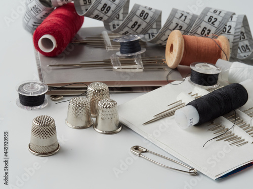 A pile of wooden buttons, a needle, old thimbles, scissors and a spool of cotton thread on a white background. The concept of needlework, sewing, tailoring