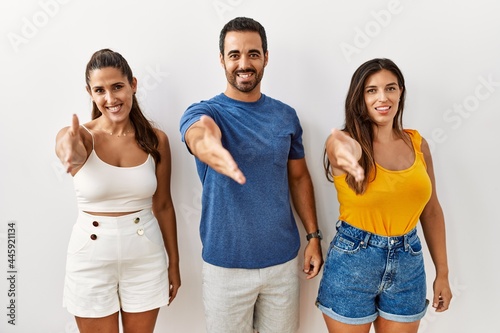 Group of young hispanic people standing over isolated background smiling friendly offering handshake as greeting and welcoming. successful business.